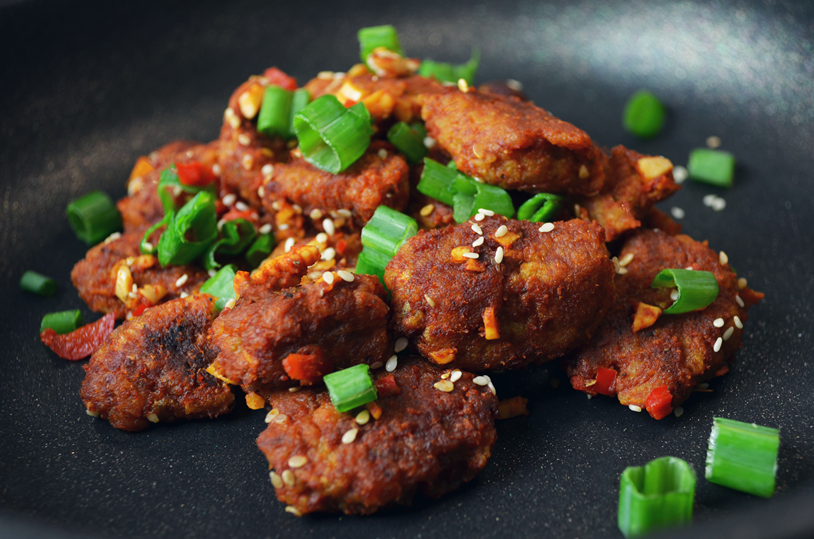 Vegan seitan pieces in chilli sauce  topped with sesame seeds and spring onions
