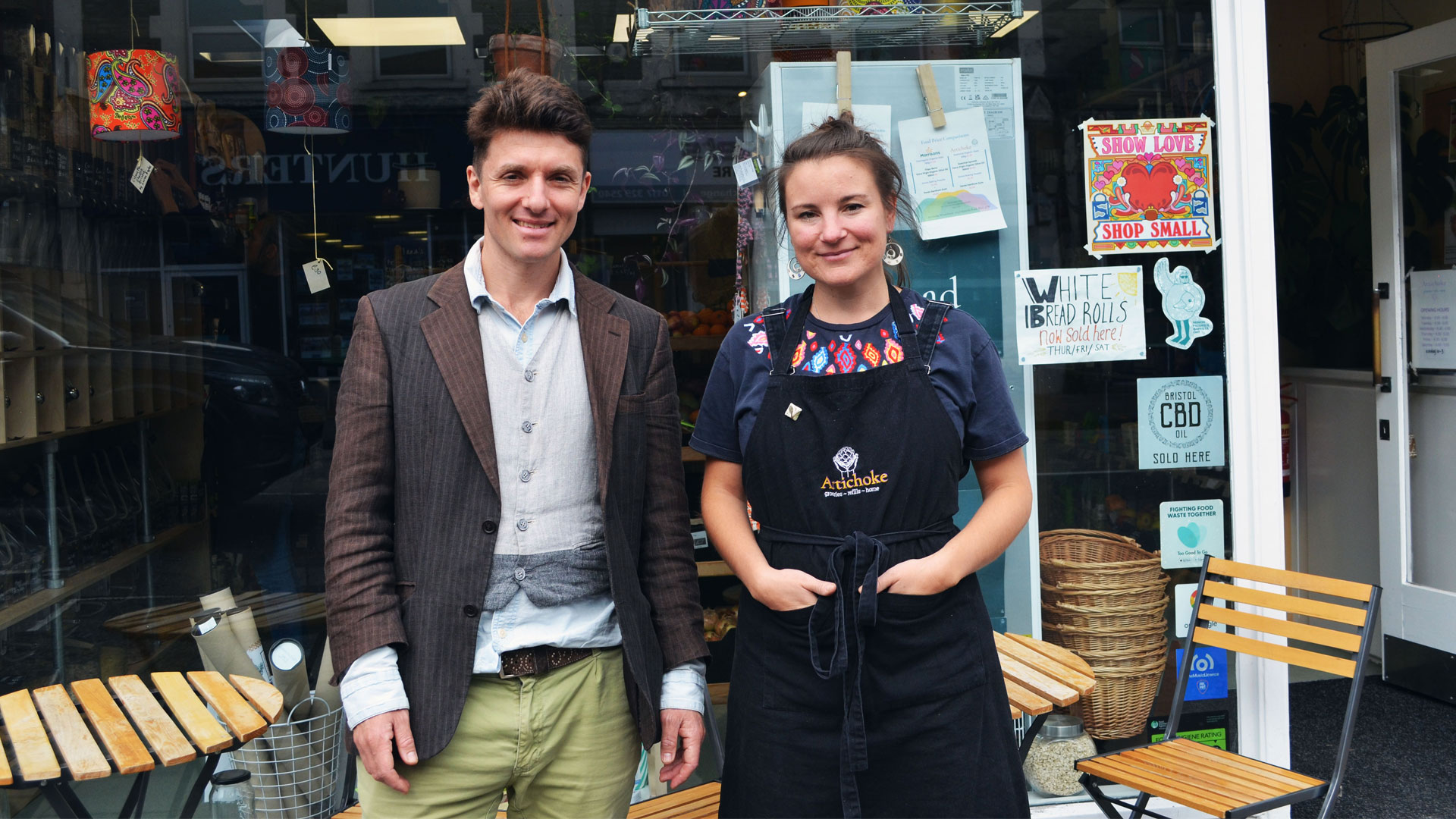 two smiling people, a man and a woman, outside their shop