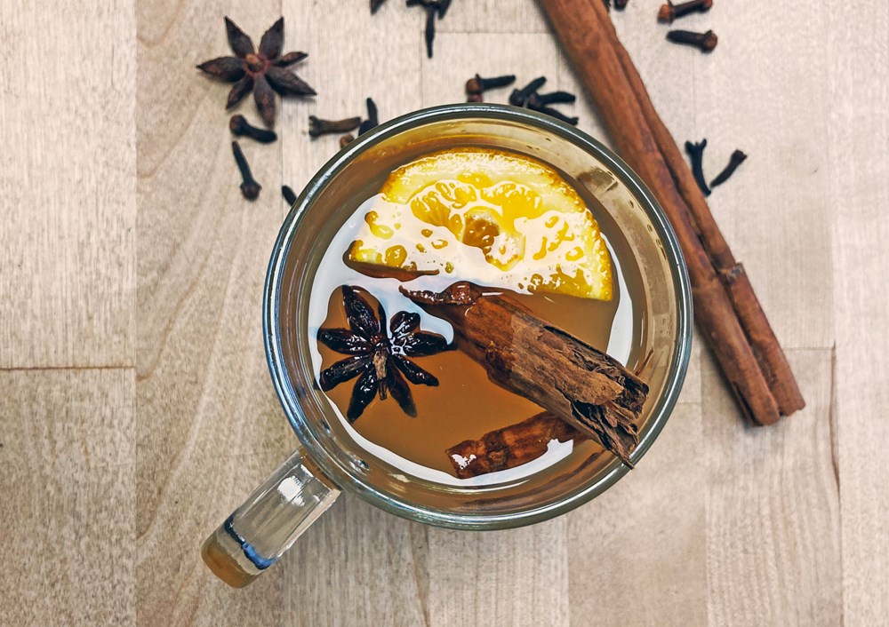glass mug filled with apple juice, cinnamon, star anise and a wedge of orange