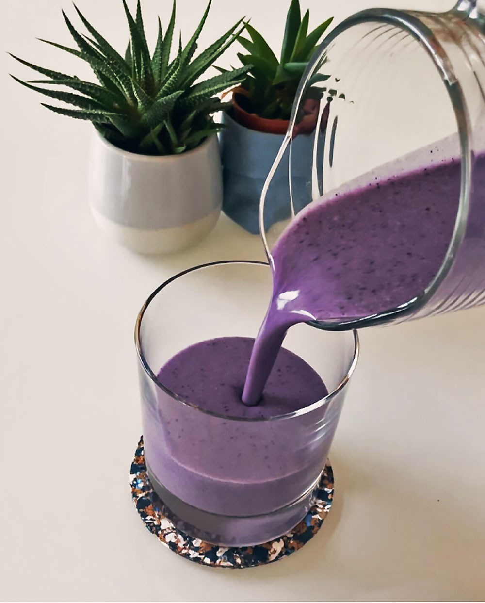 blueberry smoothie being poured in a cup with plants in the background