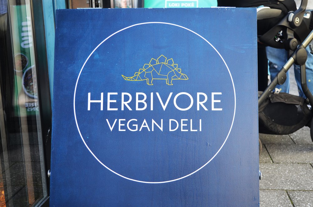 a board sign for herbivore vegan deli outside shop
